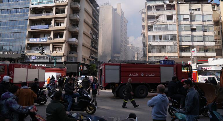 Veículos de emergência e civis reúnem-se em uma rua de Beirute em meio à fumaça e a edifícios danificados após ataques aéreos.