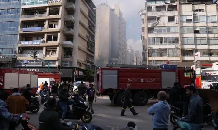 Veículos de emergência e civis reúnem-se em uma rua de Beirute em meio à fumaça e a edifícios danificados após ataques aéreos.